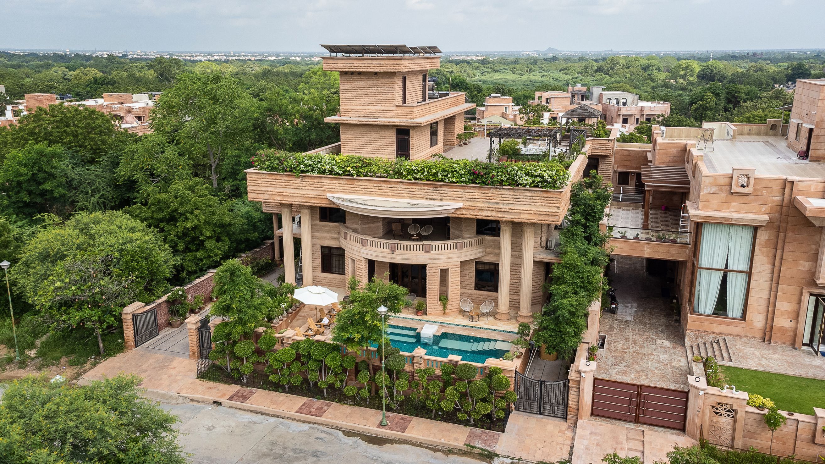 A large, multi-story building with a pool, surrounded by lush greenery and a view of the cityscape.