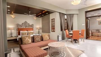 A modern hotel room with a large bed, a sofa, a dining area with orange chairs, and a ceiling fan.