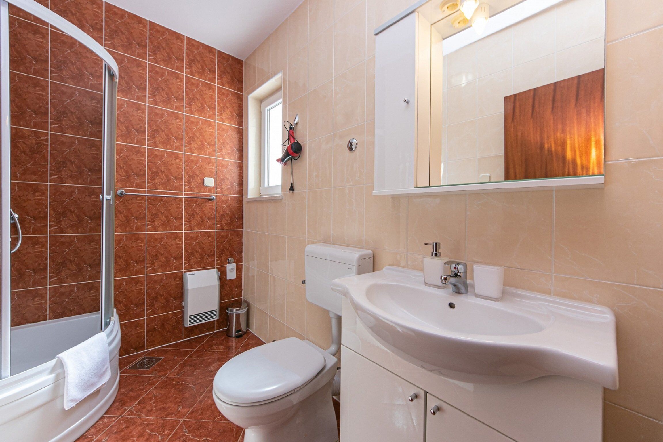 A bathroom with a shower, toilet, sink, and mirror.