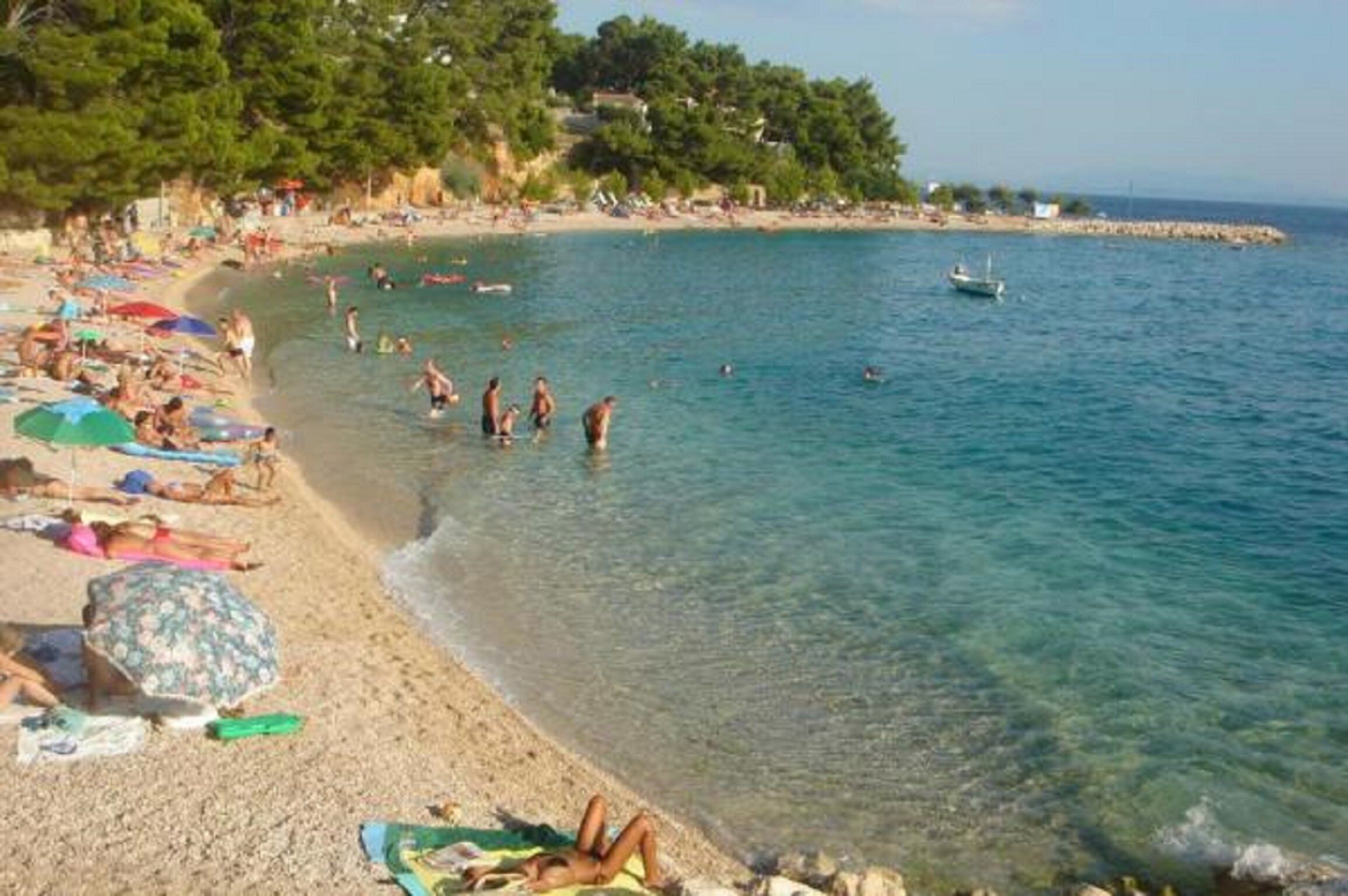 A beach with clear water, people sunbathing, and a boat in the distance.