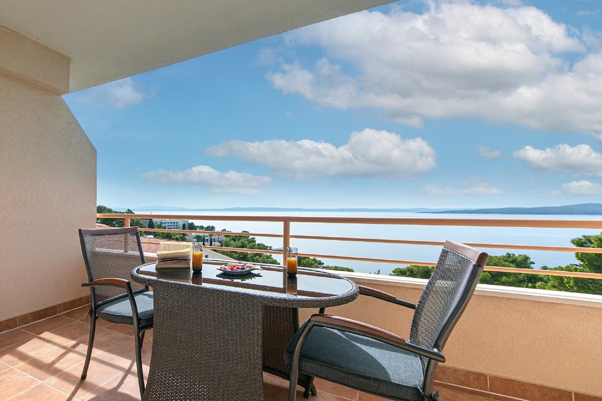 A balcony with a table and chairs, overlooking a scenic view of the sea and distant mountains.