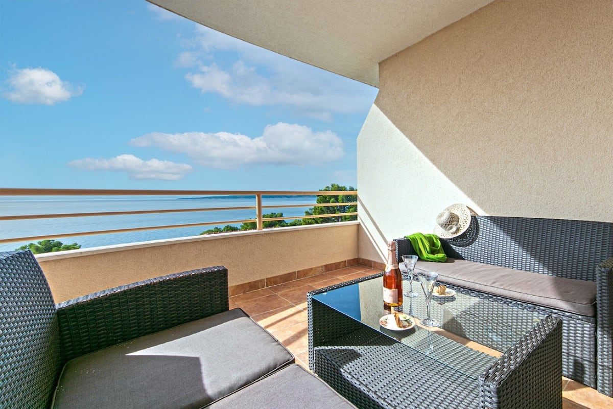 A balcony with wicker furniture, a glass table, and a bottle of wine.