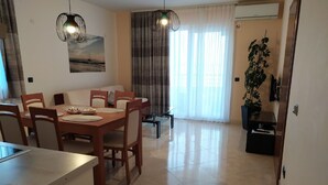 A dining area with a wooden table and chairs, a painting on the wall, and a large window with curtains. - Apartments Relax Brela (Brela)