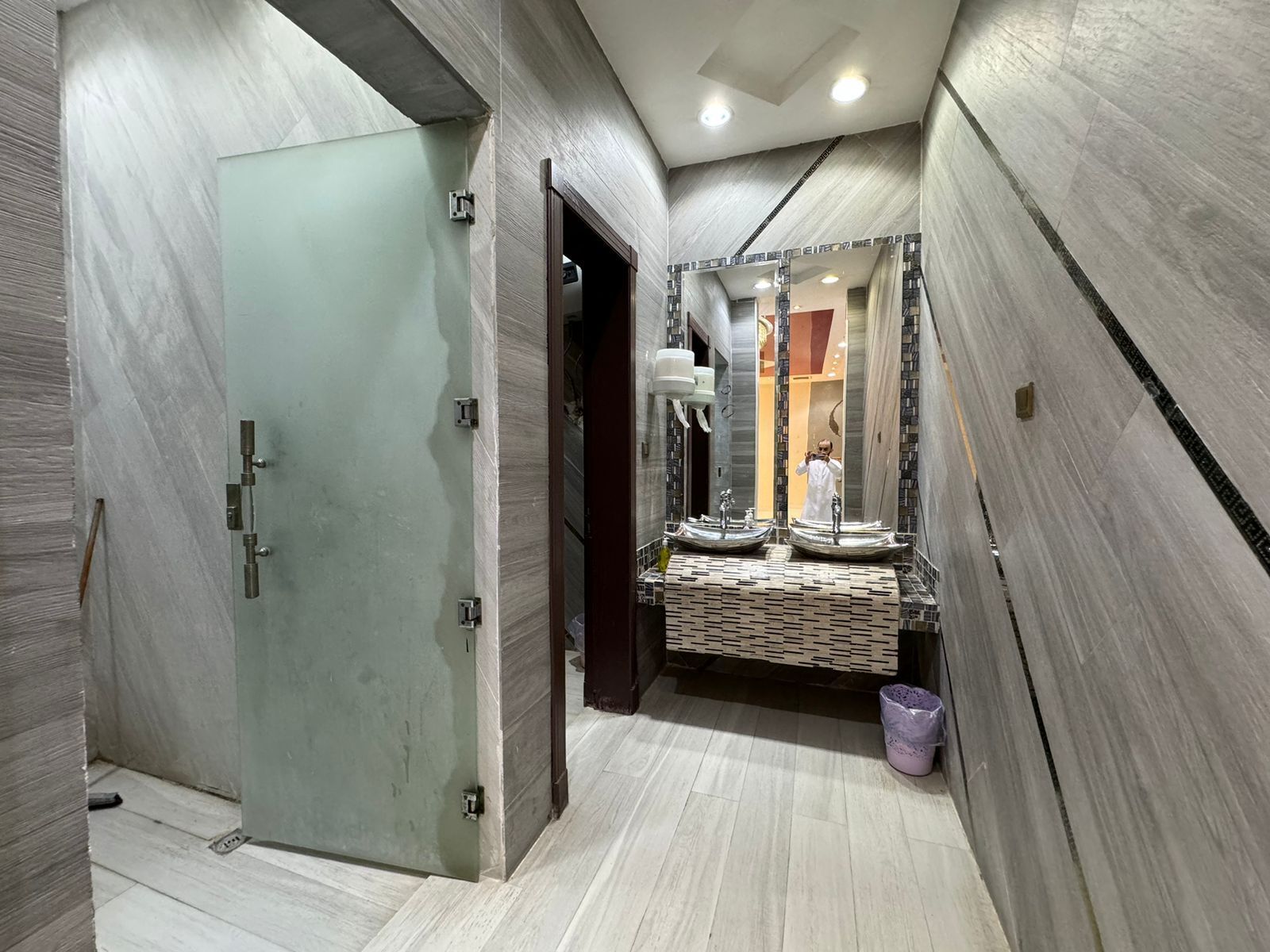 A modern bathroom with a glass door, two sinks, and a large mirror.