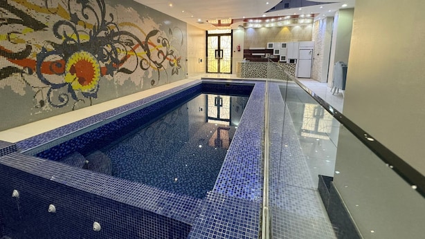 Une piscine intérieure moderne, dotée d’un mur en mosaïque et d’un espace d’accueil avec un comptoir et des sièges.