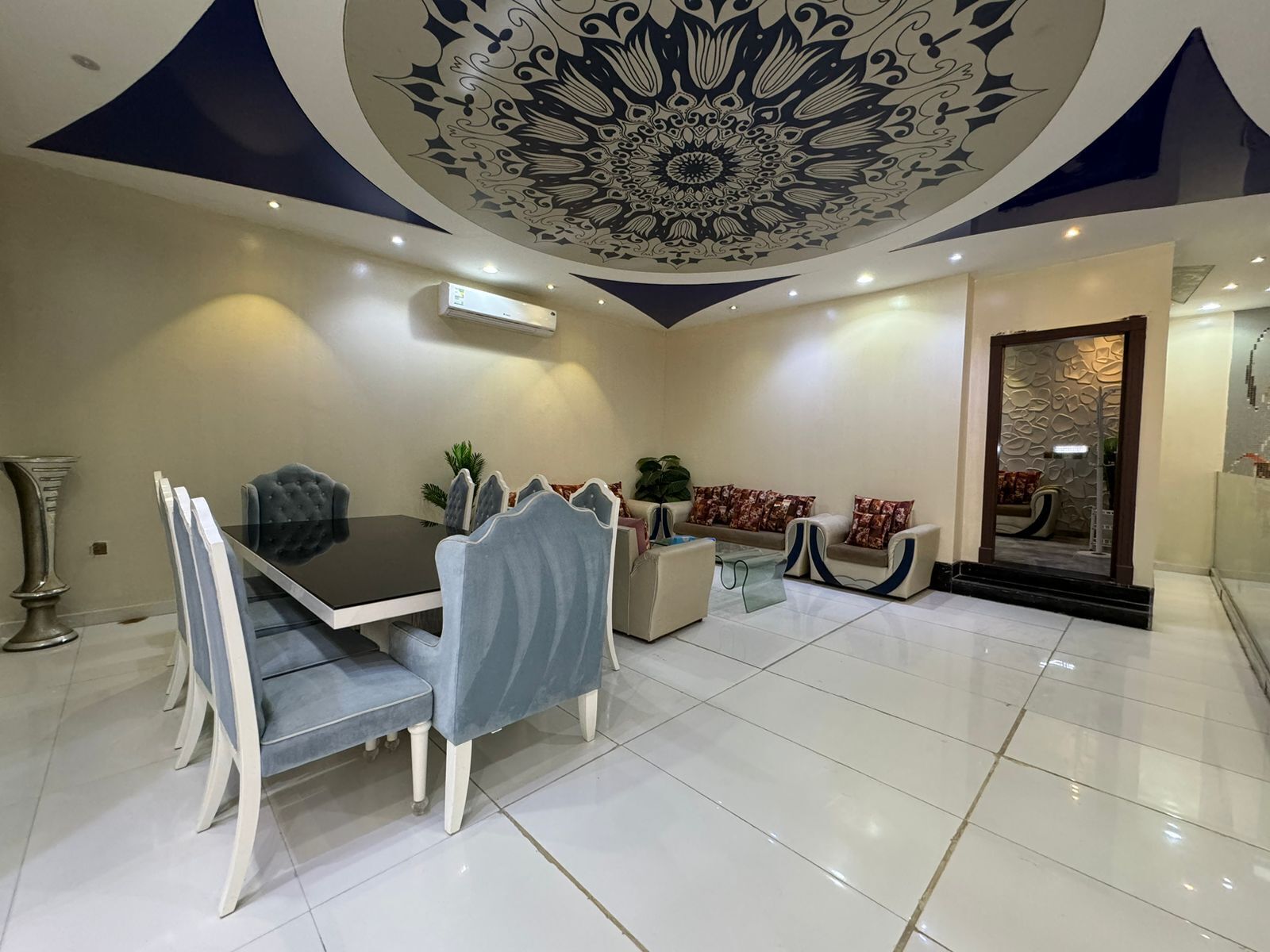 Uma sala de jantar moderna com uma mesa preta e cadeiras brancas, um sofá com almofadas estampadas e um teto decorativo.