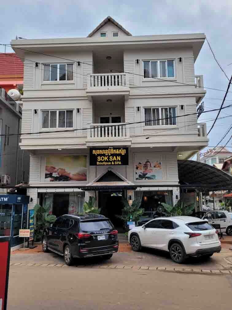 A multi-story building with a sign for 'SOK SAN Boutique & SPA'. There are cars parked in front, and the building has balconies on the upper floors.