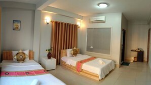 Une chambre d’hôtel avec deux lits, une grande fenêtre avec des rideaux, un climatiseur fixé au mur et une petite table avec un vase.