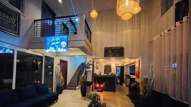 Un hall d’hôtel moderne avec un escalier, un comptoir d’accueil et un espace détente comprenant un canapé et des tables.