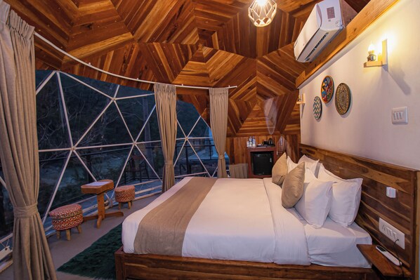 Une chambre confortable avec un grand lit, une tête de lit en bois et une vue à travers une fenêtre aux motifs géométriques.