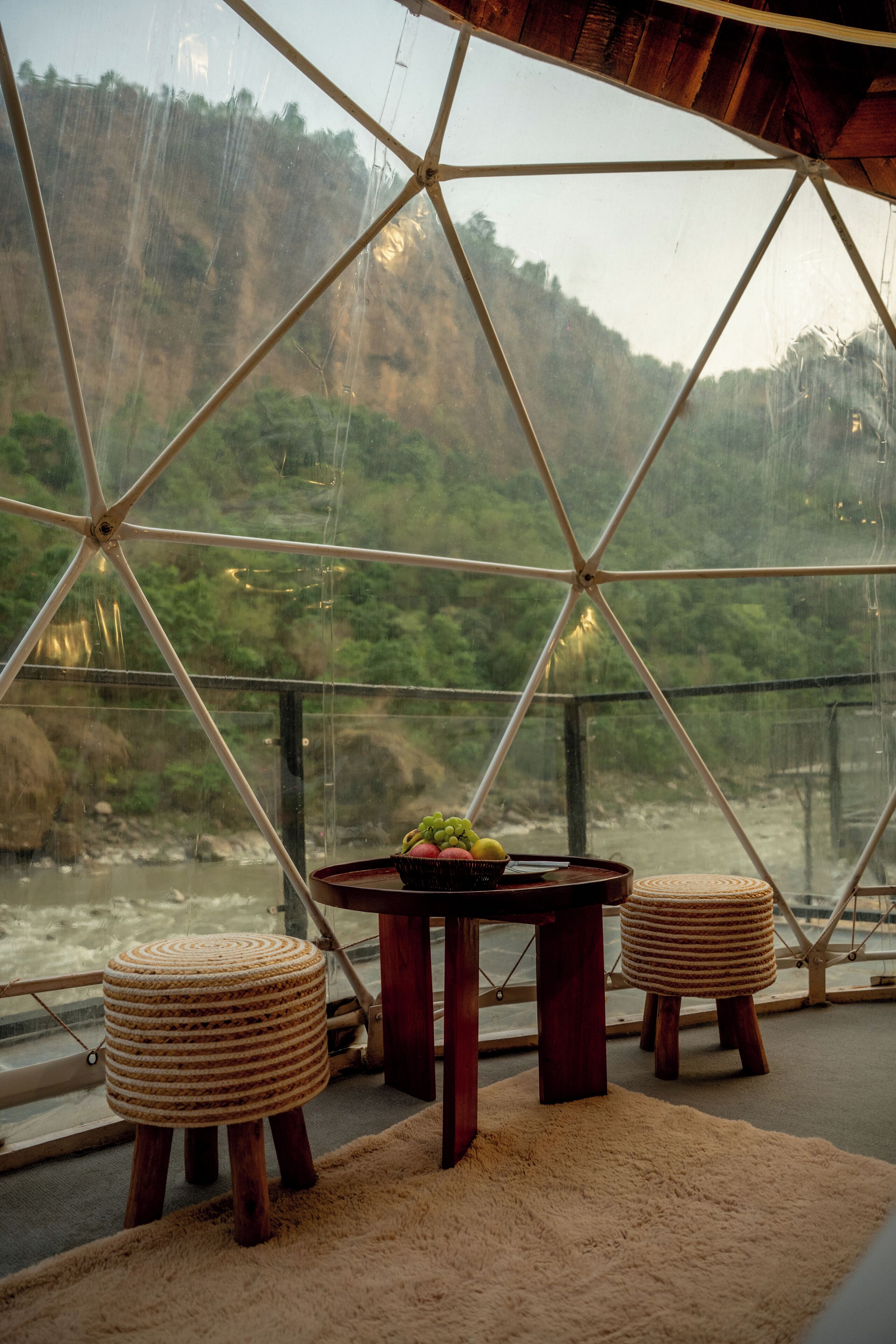A room with a glass ceiling, a table with a fruit bowl, and two woven stools.