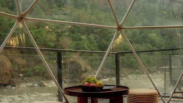 A room with a glass ceiling, a table with a fruit bowl, and two woven stools.
