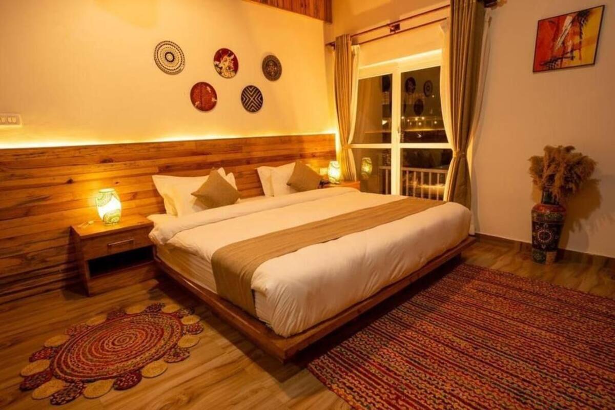 A bedroom with a wooden headboard, a large bed with white bedding, a patterned rug, and wall decor.