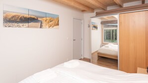 A bedroom with a wooden ceiling, a bed with white bedding, a wooden wardrobe, and a large window. - Horizon by the Sea by Interhome (Renesse)