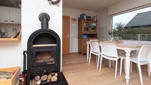 A modern kitchen with a wood-burning stove, white brick walls, a dining area with white chairs, and a view of the outside. - Horizon by the Sea by Interhome (Renesse)