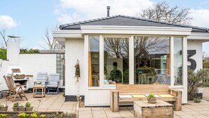 A modern house with a large glass conservatory, a wooden deck, and a garden with yellow flowers. - Horizon by the Sea by Interhome (Renesse)