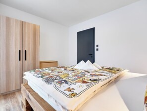 A bedroom with a bed, a wooden wardrobe, a dark door, and a small bedside table. - Beautiful apartment for 6 people with A/C, WIFI, TV and patio (Ostrov)