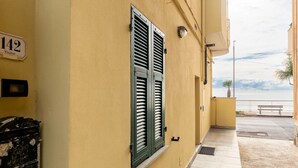 Un bâtiment à la façade jaune, une fenêtre avec des volets verts et une plaque portant le numéro « 142 ».