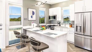 Une cuisine moderne dotée d’un îlot central, d’appareils électroménagers en acier inoxydable et de grandes fenêtres.