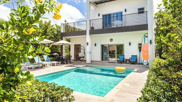 Un bâtiment moderne à deux étages doté d’une piscine, d’un espace extérieur aménagé et d’un balcon.