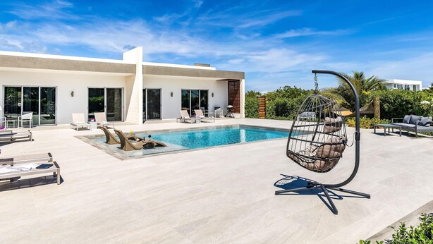 A modern pool area with a hanging chair, lounge chairs, and a clear blue sky.