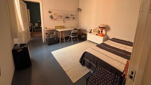 Una camera da letto con un letto, una scrivania, una sedia e un angolo cottura.
