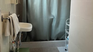 Un bagno con tenda doccia, lavandino, water e tappetino verde.