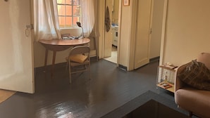 Una stanza con un tavolo da pranzo, una sedia, un divano e una zona cucina visibile attraverso una porta aperta.