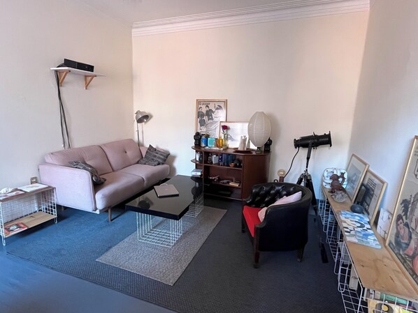 A living room with a sofa, a coffee table, a bookshelf, a lamp, and a small table with a fan.