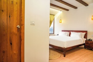 Een slaapkamer met een houten deur, een bed met witte beddengoed, een nachtkastje en een lamp.