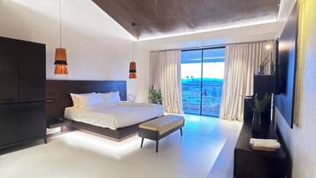 A modern bedroom with a large bed, a bench, a TV, and a view of the outdoors.