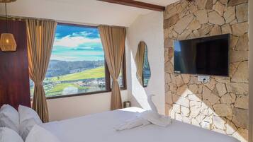 A hotel room with a large bed, a stone wall, a TV mounted on the wall, and a window with curtains.