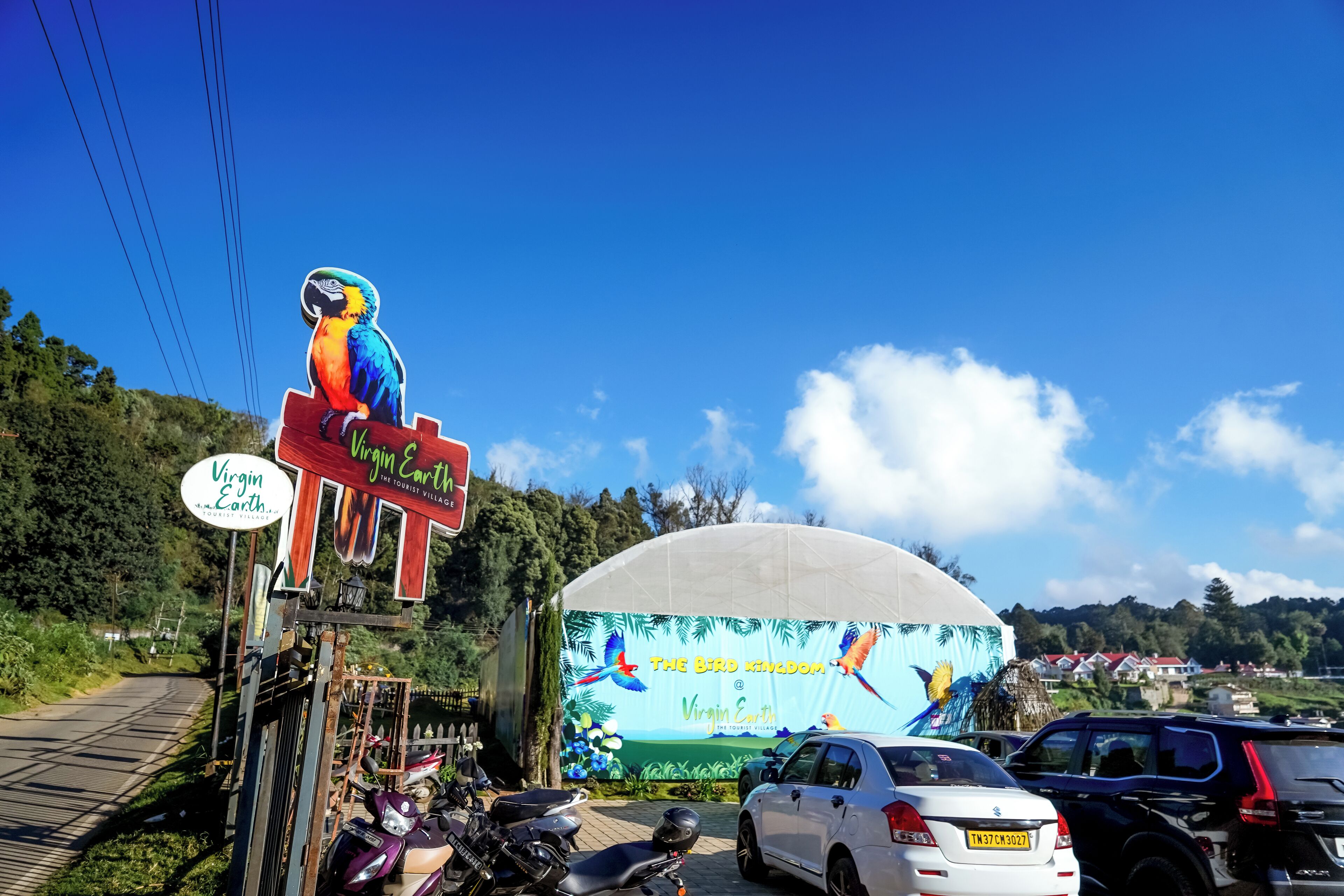 A sign for 'Virgin Earth' with a parrot and a large billboard in the background advertising 'The Bird Kingdom'.