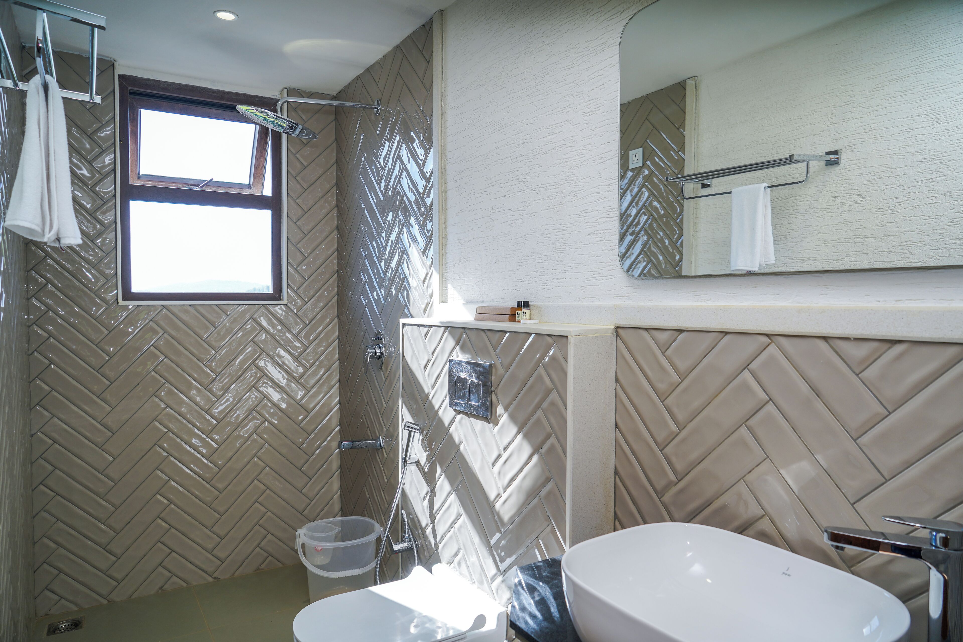 A bathroom with a herringbone tile pattern, a large mirror, a sink, and a shower area.
