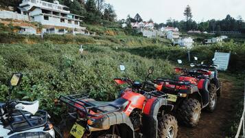 A row of ATVs parked on a dirt path with houses in the background.