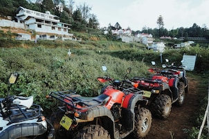 A row of ATVs parked on a dirt path with houses in the background.