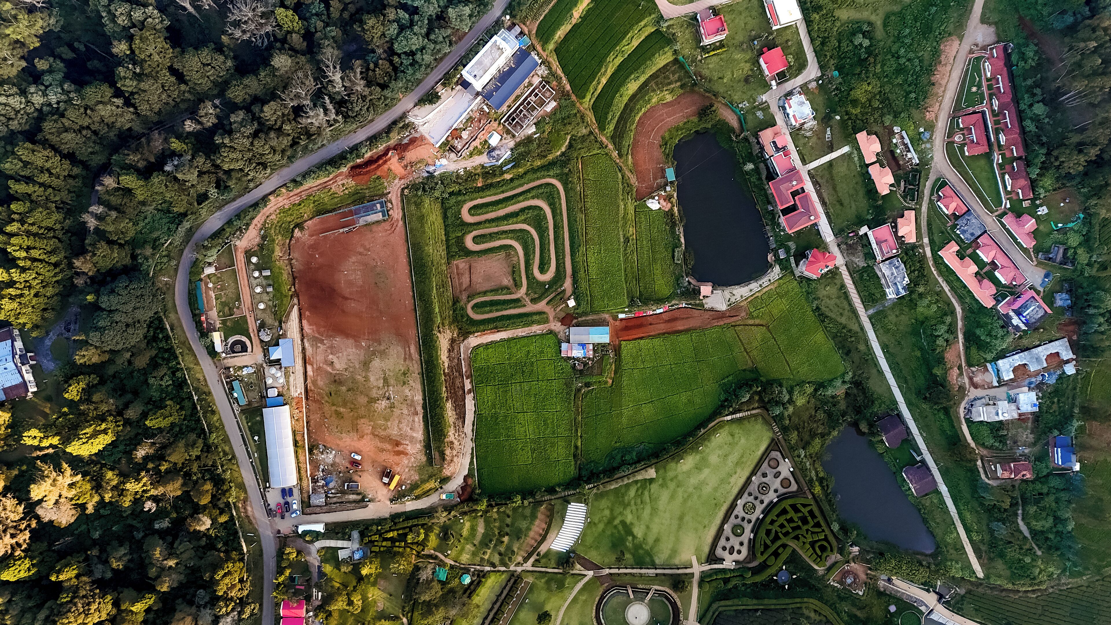 An aerial view of a park with a large pond, walking paths, and several buildings with red roofs.