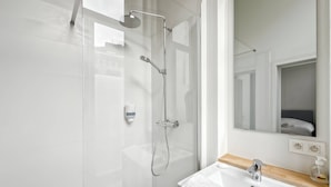 Une salle de bain moderne avec une douche à l’italienne en verre, un lavabo blanc doté d’un plan de travail en bois et un miroir au-dessus du lavabo.