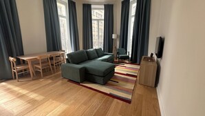 Un salon moderne avec un canapé d’angle, une table à manger en bois et des chaises, ainsi qu’un téléviseur fixé au mur.