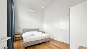 Une chambre moderne avec un lit gris, un plancher en bois, un appareil de climatisation blanc et une porte.