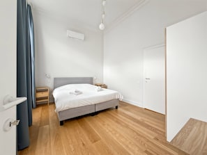 Ein modernes Schlafzimmer mit einem grauen Bett, Holzboden, einer weißen Klimaanlage und einer Tür.