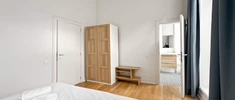 A modern bedroom with a large bed, a wardrobe, a small table, and a bathroom visible through an open door.