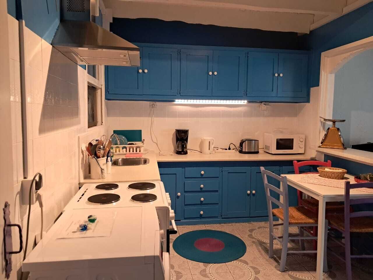 A compact kitchen with blue cabinets, a white stove, and a dining area with a table and chairs.