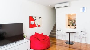 A modern living room with a flat-screen TV, a red bean bag, and a dining area with a small table and chairs. - Oversized Designer Warehouse in Surry Hills / City (Surry Hills)
