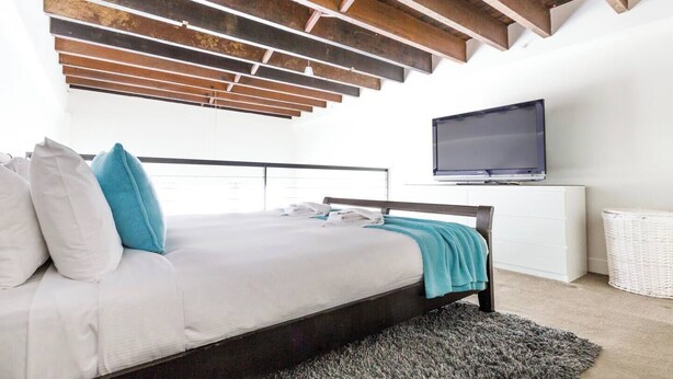 A bedroom with a bed, pillows, a TV, and a white cabinet. - Oversized Designer Warehouse in Surry Hills / City (Surry Hills)