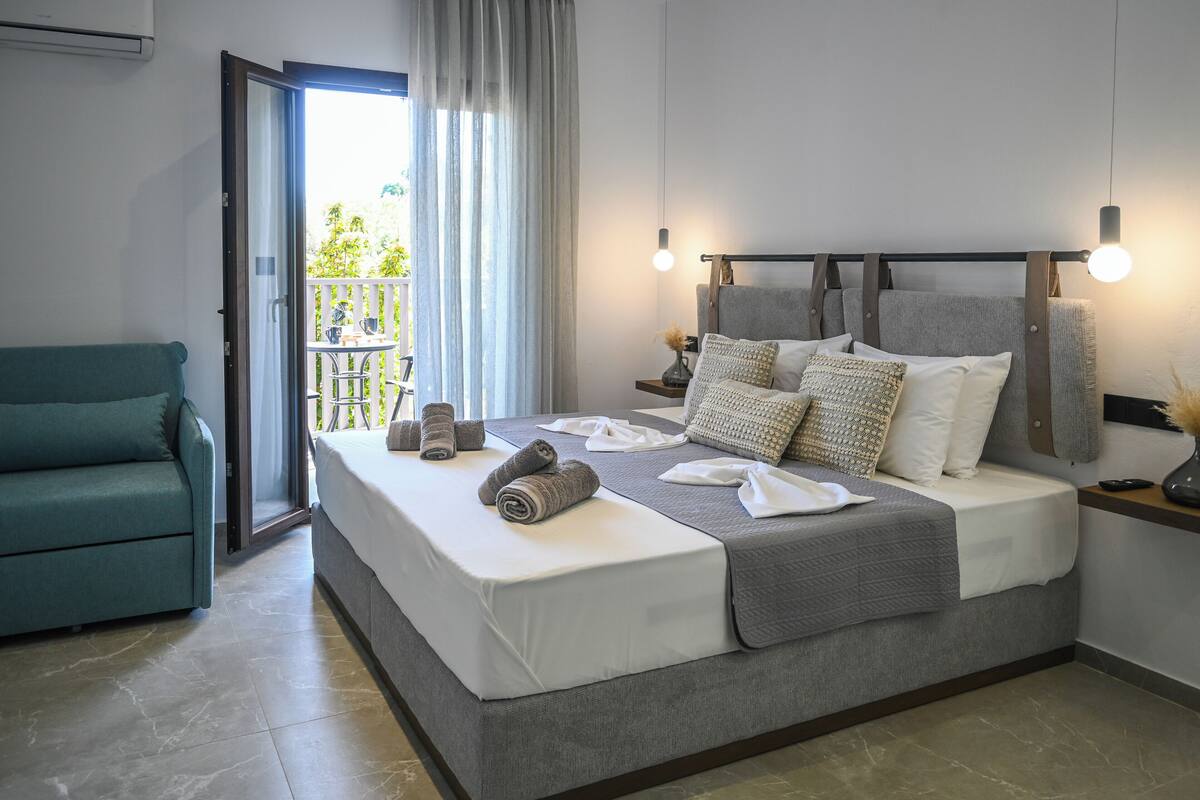 A modern bedroom with a large bed, a sofa, and a balcony view.