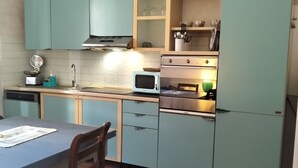 A compact kitchen with teal cabinets, a microwave, a stove, and a sink.