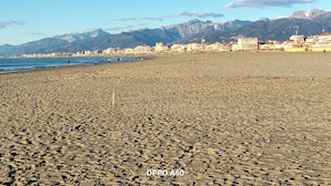 A beach with rocky terrain, a clear sky, and mountains in the background.