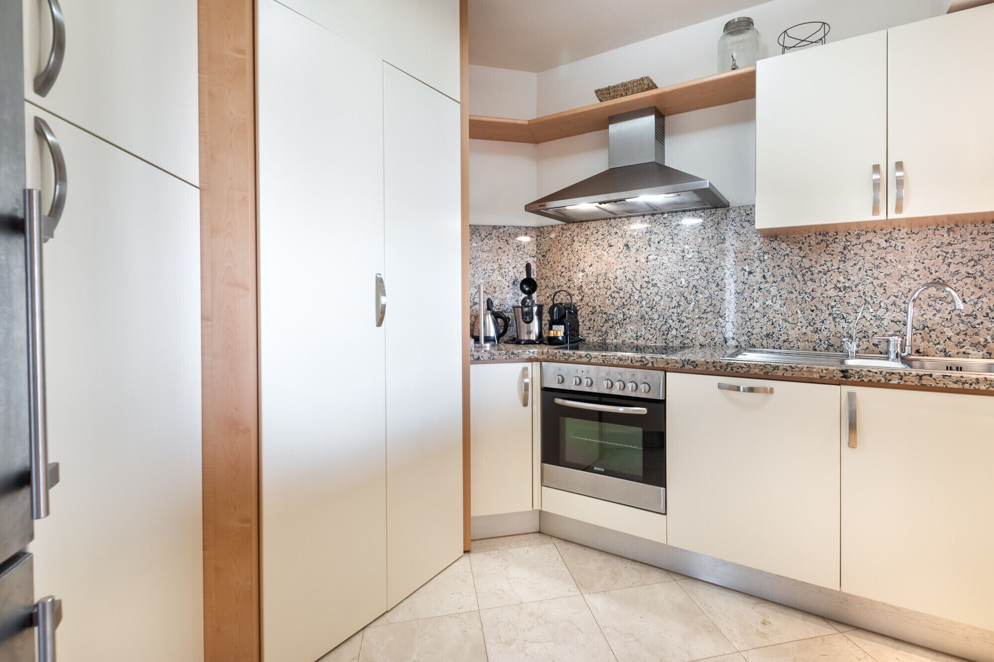 A modern kitchen with white cabinets, a Bosch oven, granite countertops, and a stainless steel range hood.