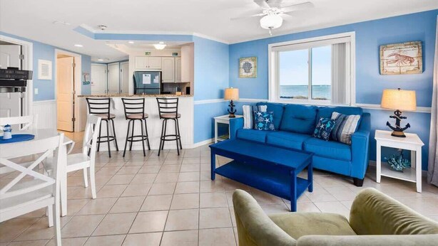 Un salón con sofá azul, comedor con sillas blancas y cocina al fondo.
